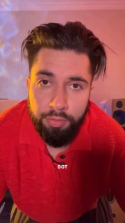 Портрет в три четверти: мужчина в красной рубашке сидит в студии звукозаписи, на заднем плане акустические колонки и монитор с визуализацией аудиофайла.