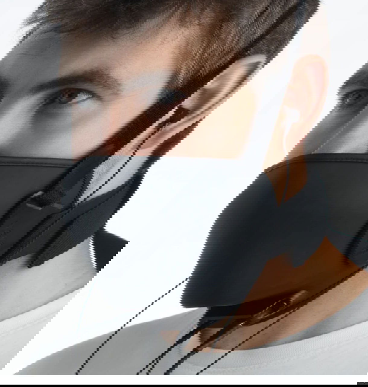 Мужчина в белой футболке носит маску Vekta: видна посадка на лице, ремни и проводные наушники или микрофонные разъёмы.