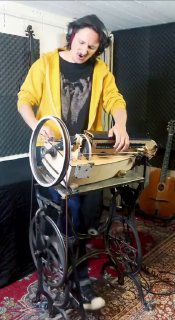 Крупный план исполнения: руки на лире, металлическая катушка и элементы механики на основании старой швейной машины Singer.