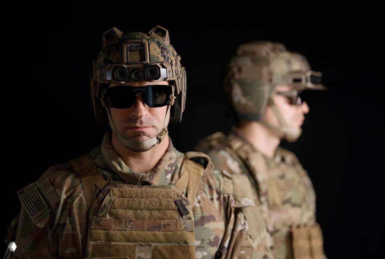 Два солдата в камуфляжных формах в шлемах Anduril EagleEye на темном фоне; видны оптические сенсоры, защитные очки и часть экипировки.