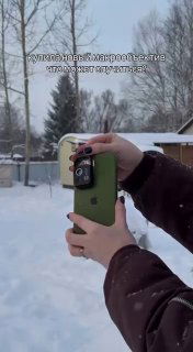 Человек держит смартфон с накрученным макрообъективом на морозном фоне — сцена съёмки снежинок на улице в зимнем дворе.