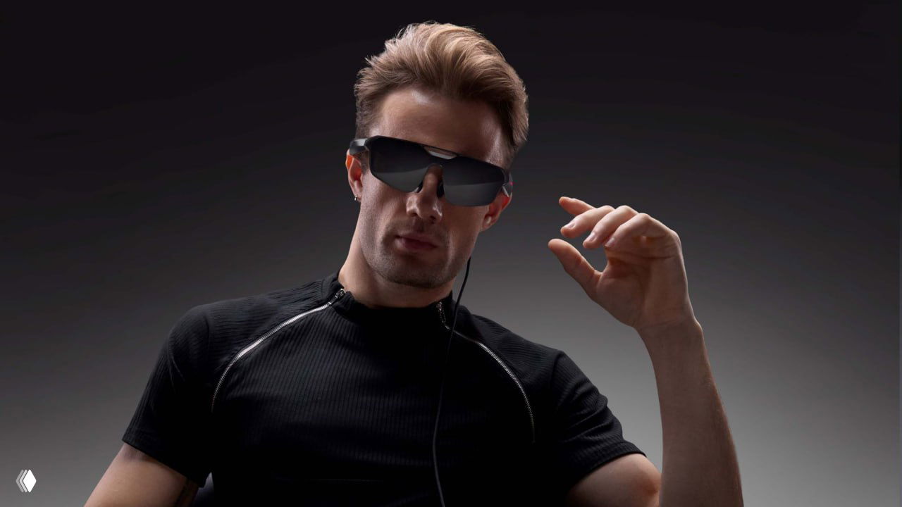 Портретный кадр мужчины в игровых очках Asus на нейтральном фоне — видно форму и дизайн девайса с тёмными линзами.