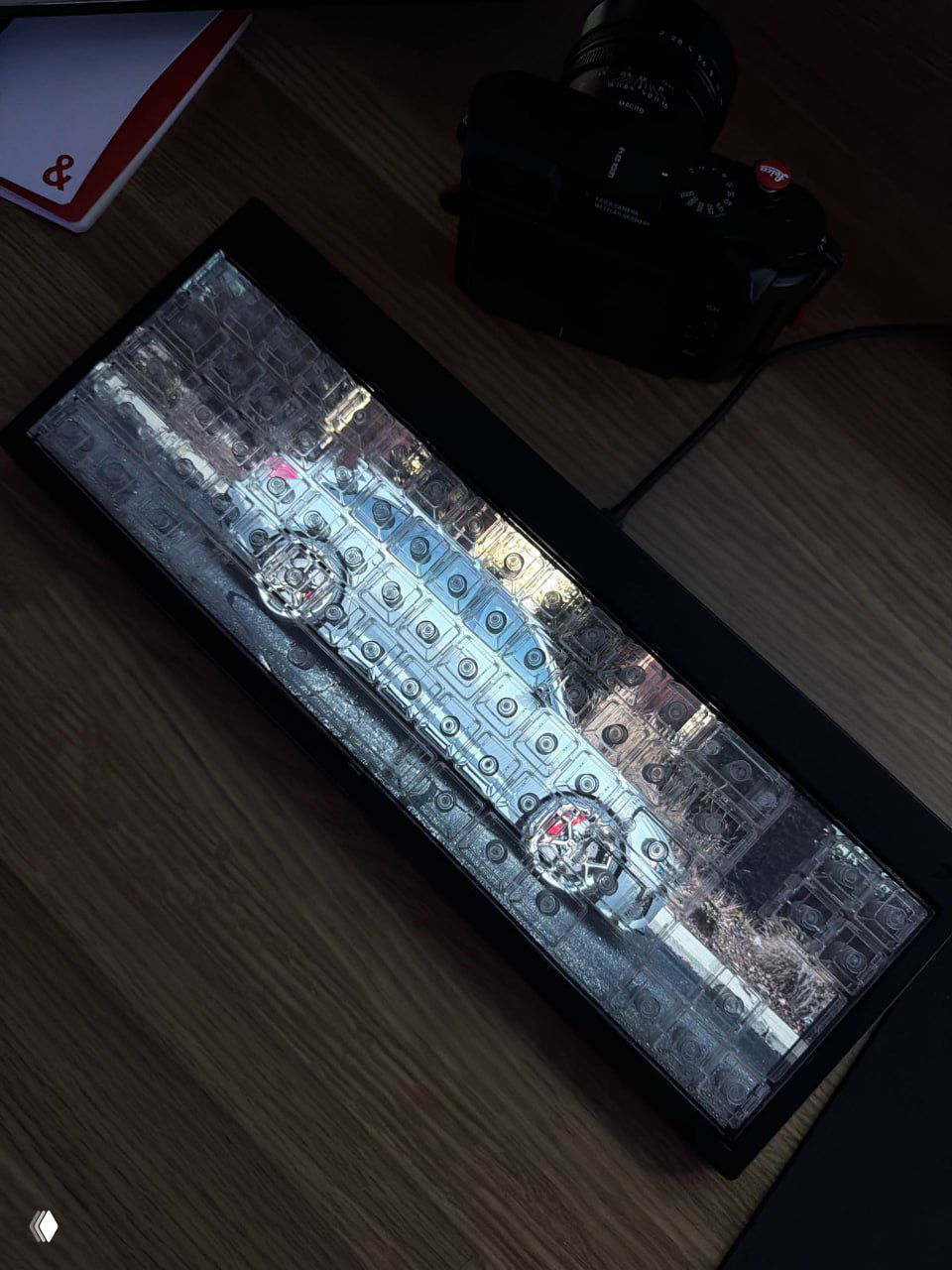 Наклонный снимок клавиатуры Centerpiece на деревянном столе рядом с фотоаппаратом; видны прозрачные колпачки и интегрированное видеодисплейное поле.