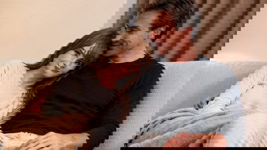 Emily сидит на диване рядом с мужчиной — показ взаимодействия и выражения эмоций у человекоподобного робота в бытовой сцене.