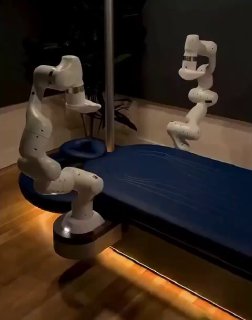 Белая роботизированная рука iYU рядом с массажной кушеткой в затемнённой комнате — демонстрация гибкого робота-массажёра.