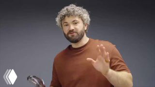 Кадр из видео: блогер приветствует камеру, на заднем плане виден робот Unitree и обстановка демонстрации эксперимента с пистолетом.