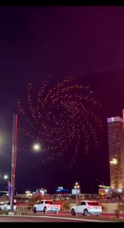 Ночное небо над Лас-Вегасом, дроны формируют светящуюся спираль — кадр шоу с видимыми городскими огнями и башнями.