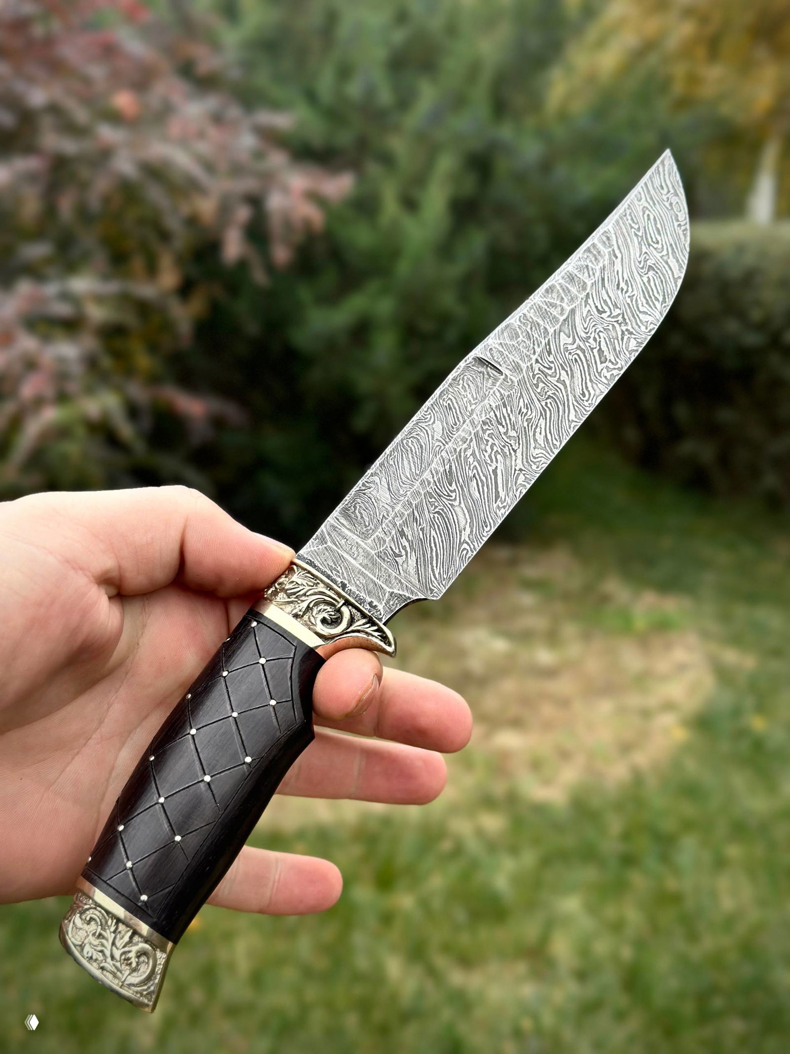 Крупный кадр одного ножа: характерный рисунок дамаска на лезвии и инкрустированная рукоять из граба с мелкими декоративными шпильками.