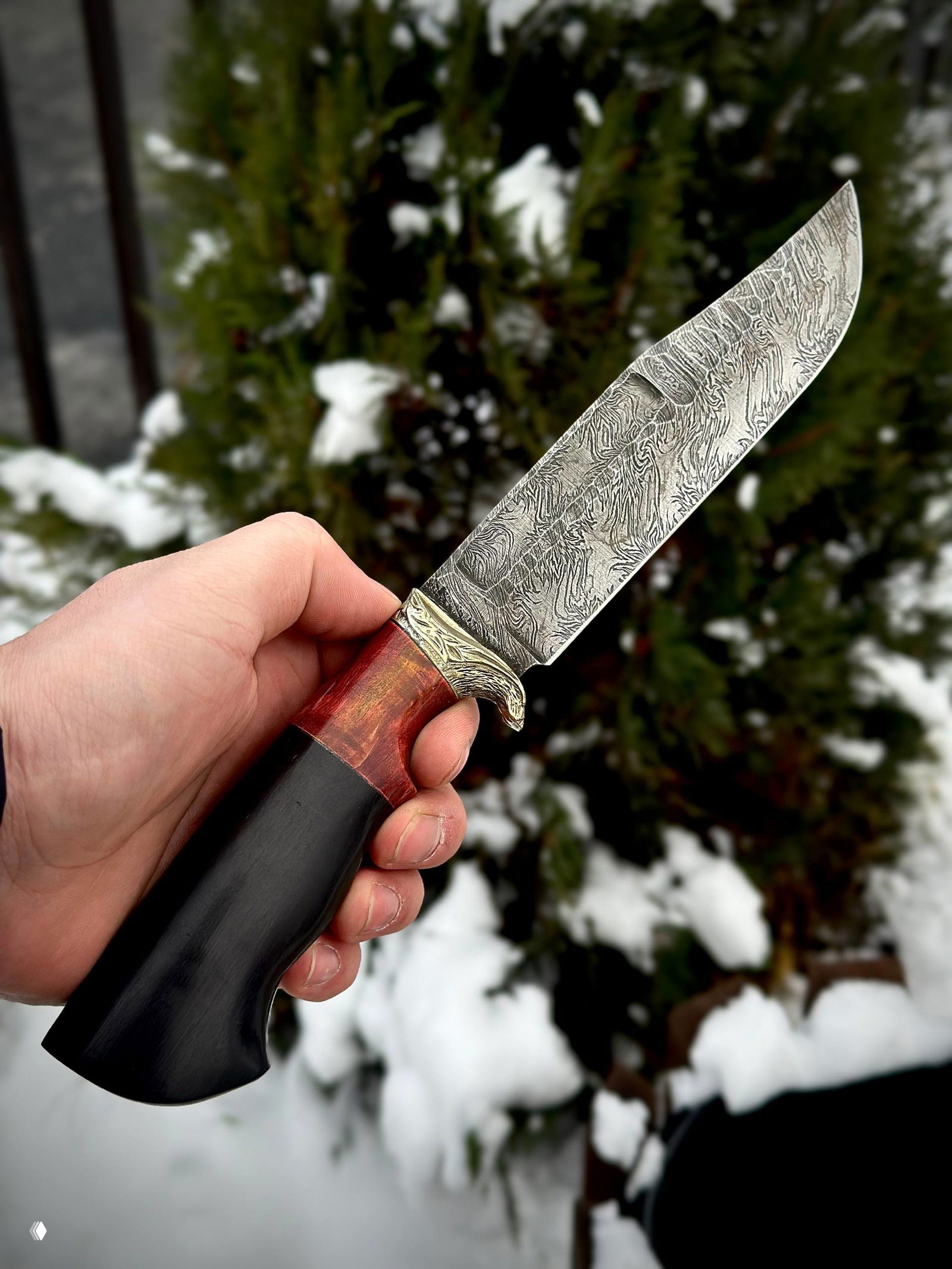 Крупный план клинка из дамаска с большим увеличением рисунка и гардой; в фокусе текстура металла и переход к рукояти с красной вставкой.