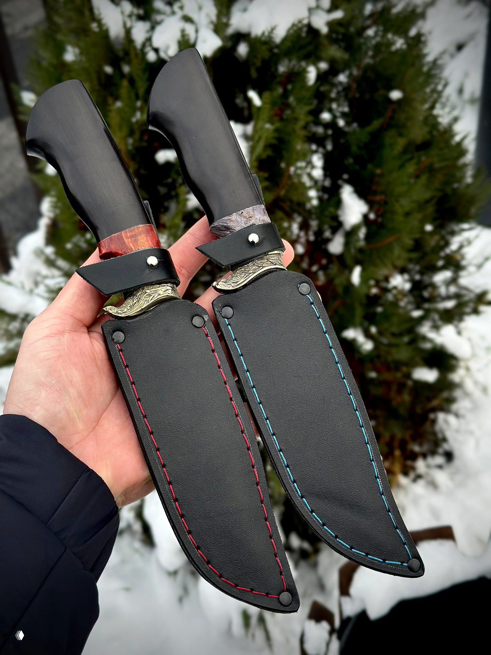 Два кожаных ножен с контрастной прострочкой в руках владельца; показать как смотрятся ножи в комплекте с ножнами на фоне снега.