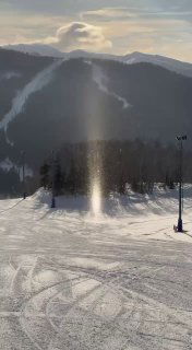 Широкий план лыжной равнины с сияющей колонной ледяных кристаллов и вечерним небом над курортом «Горный воздух», видны следы катания.