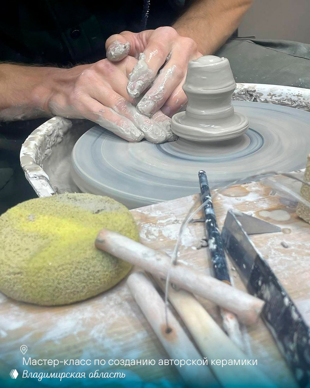 Руки мастера на гончарном круге формуют изделие из глины; инструменты и губка рядом — сцена мастер‑класса по керамике.