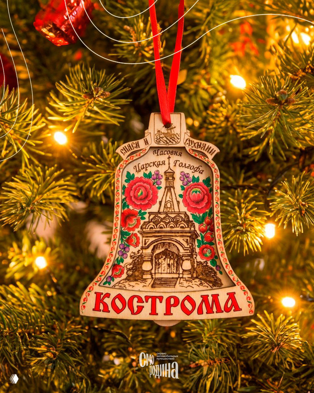 Деревянный колокольчик-брелок с полховско‑майданским орнаментом и крупной надписью «Кострома», висящий на еловой ветке среди гирлянд и игрушек.