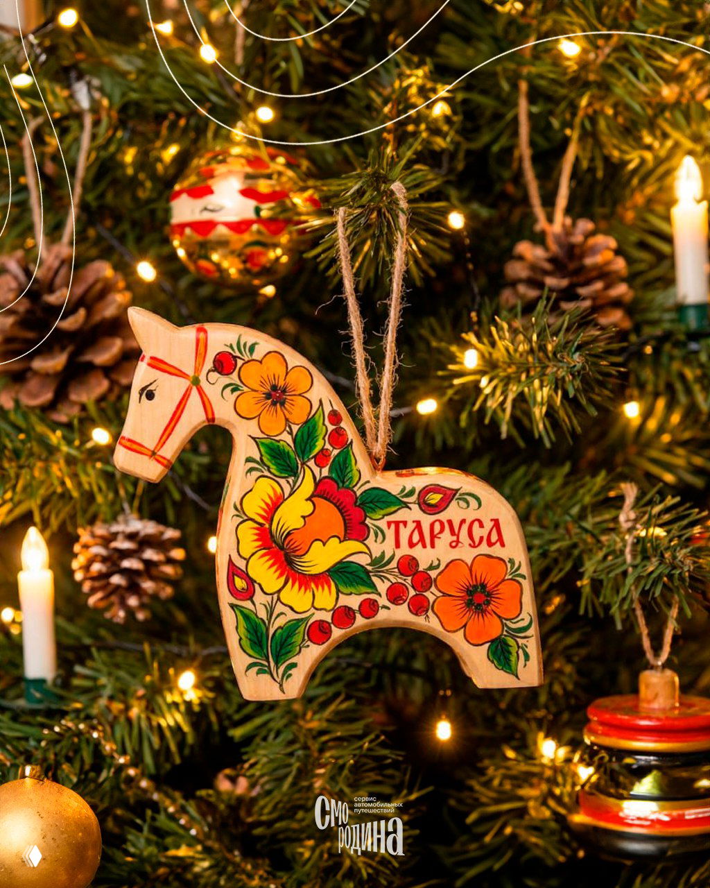 Деревянная фигурка лошадки с яркими цветочными узорами в стиле Полховско‑Майданской росписи и надписью «Таруса», украшенная на рождественской ёлке с шишками.