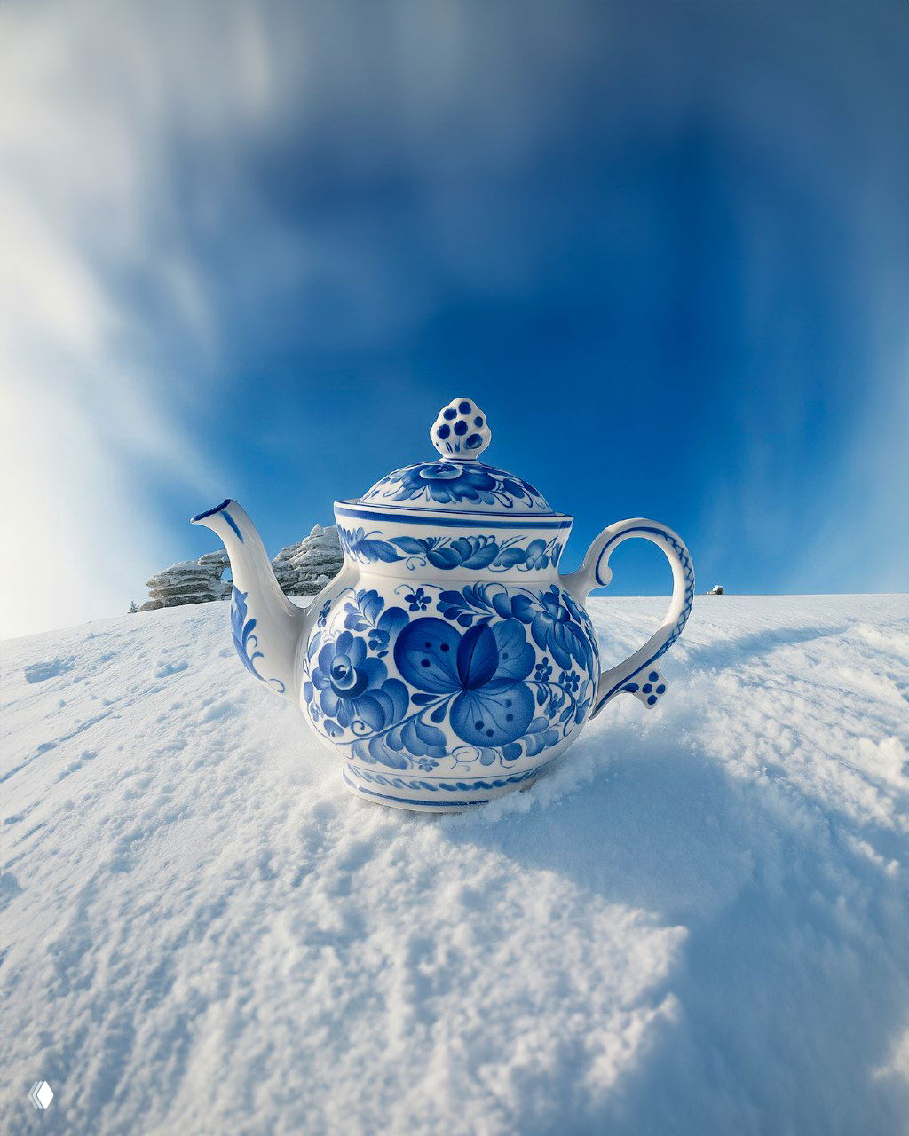 Чаевник в стиле гжель, поставленный на снег: керамический сосуд с сине-белым орнаментом на фоне зимнего пейзажа и голубого неба.