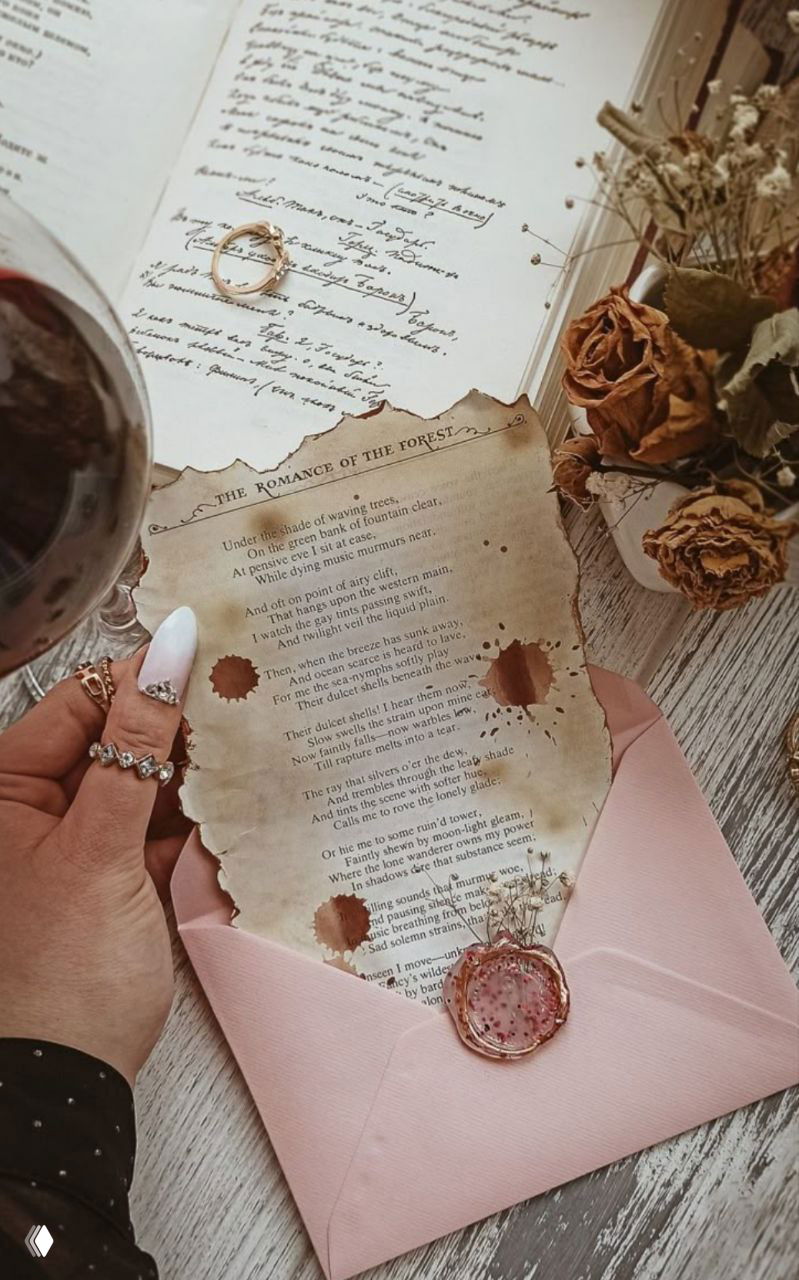 Рука держит состаренный лист с текстом в розовом конверте на деревянном столе; рядом сухие розы, кольца и бокал, создавая атмосферу личного послания и ритуала