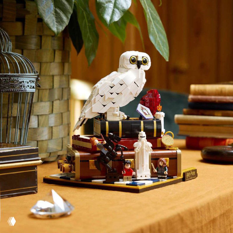 Крупный план демонстрационного стола с элементами набора LEGO: белая сова, мини-сценки из первой части фильма, шахматные фигуры и прочие мелкие детали.