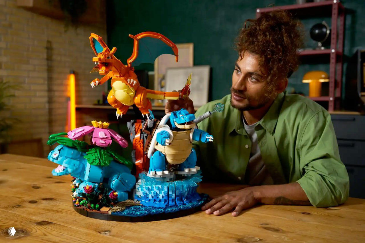 Большая диорама Lego с Венузавром, Чаризардом и Бластойзом на подставке; человек рядом рассматривает и показывает фигурки в студийной обстановке.