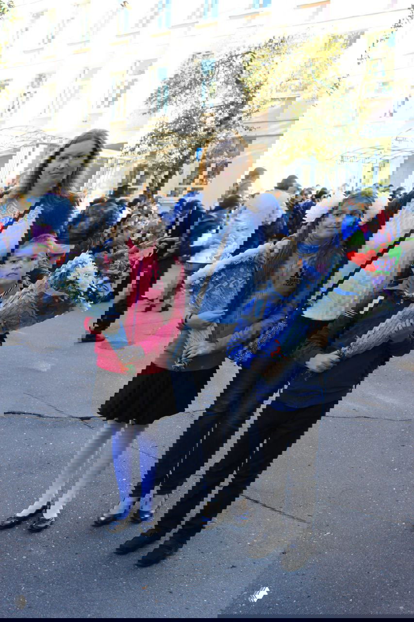 Мать с двумя детьми на школьной линейке с букетами цветов: начало учебного года, дети в школьной форме или повседневной одежде на заднем дворе школы.