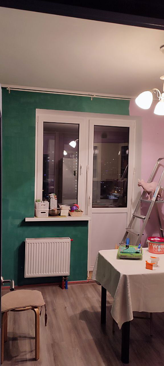 Интерьер кухни в процессе ремонта: глубокий бутылочно-зелёный участок стены, стол, стремянка и вечерние огни за окном — смена цветовой палитры дома.