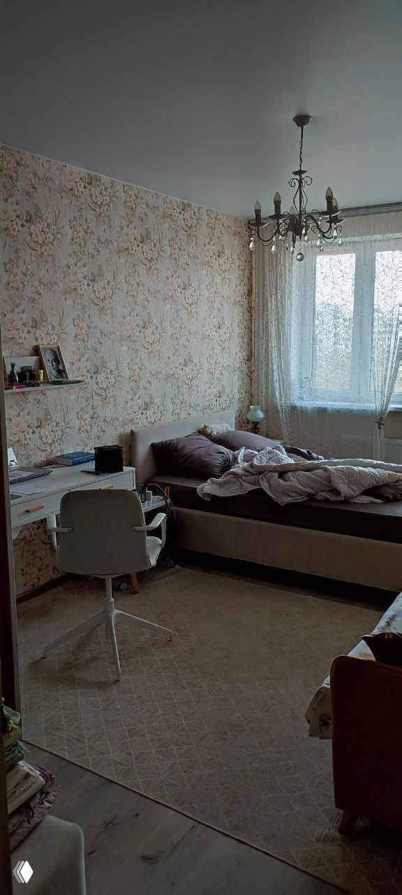 Спальня с кроватью, рабочим столом, винтажными обоями и люстрой; виден беспорядок постели — этап ремонта и исцеления.