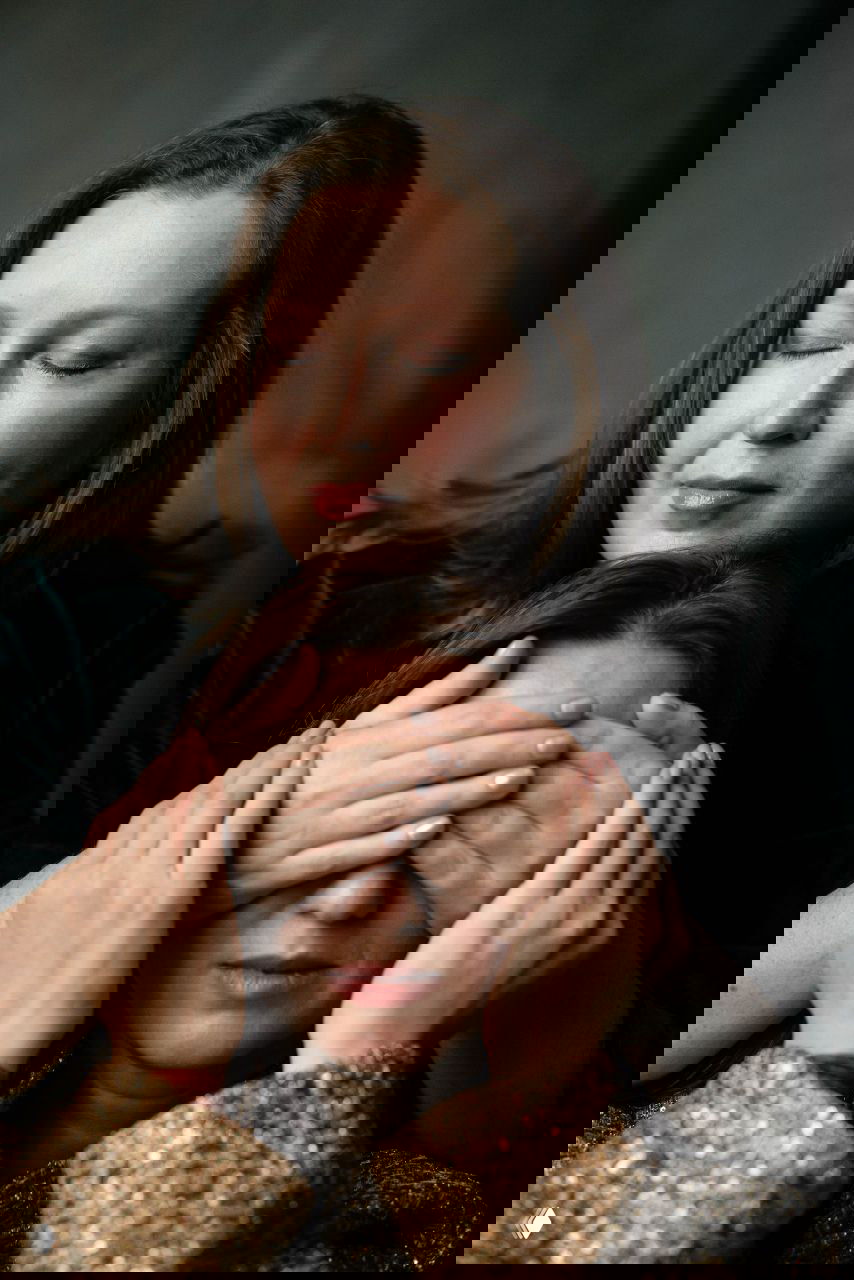 Интимный портрет: одна женщина закрывает глаза другой руками, сцена доверия и заботы в мягком студийном свете.