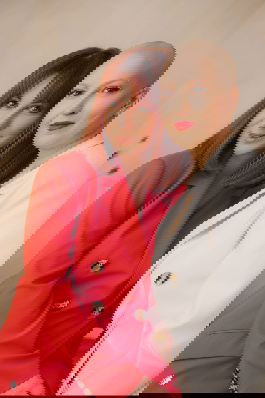 Близкий портрет двух подруг, одна с бритой головой, обе в пиджаках — тема поддержки, женской солидарности и принятия внешности.