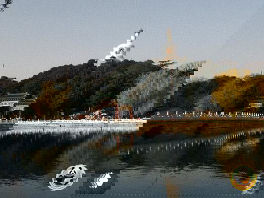 Пейзаж парка в Пекине с озером и белой пагодой на холме, отражение в воде и спокойная прогулочная атмосфера рядом с памятником.