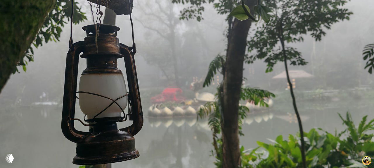 Подвесная лампа на переднем плане и тихий туманный пруд с лодками и декоративной скульптурой дракона в центре озера парка Байхуань.