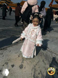 Маленькая девочка в традиционном китайском костюме на территории Запретного города, улыбается и стоит в окружении туристов.