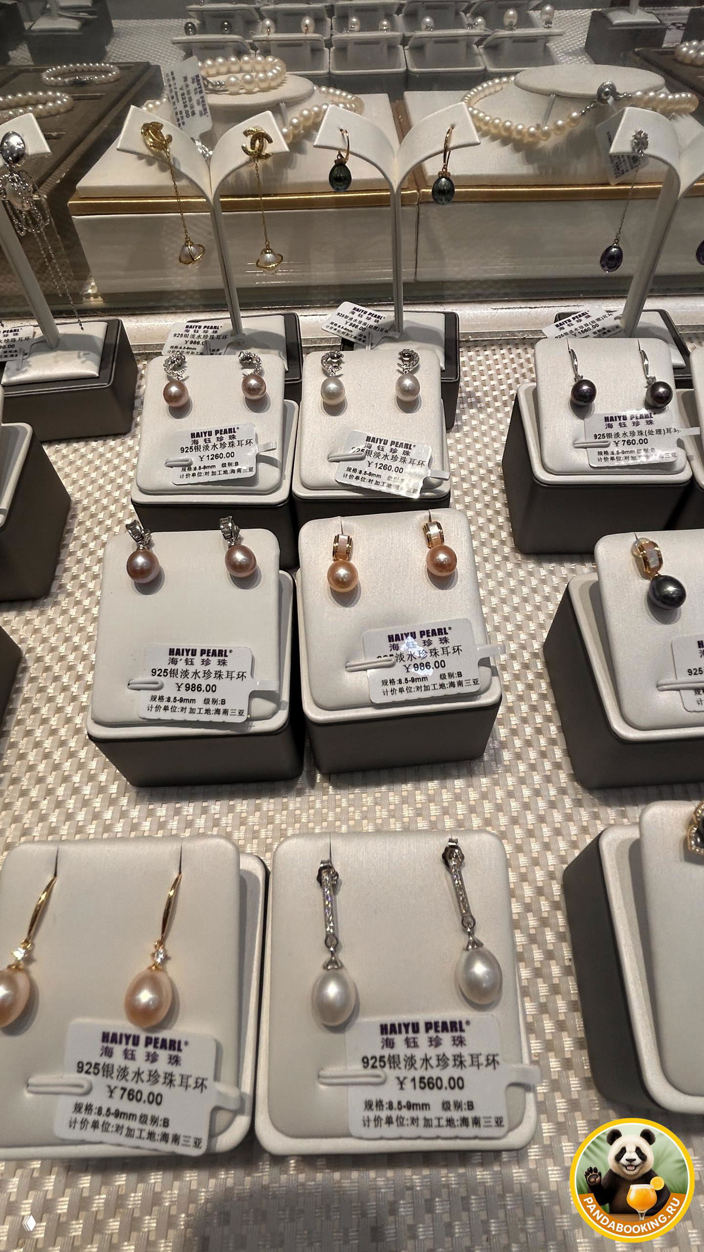 Фрагмент витрины с рядом боковых подставок, на которых аккуратно размещены серьги с жемчугом разных оттенков и стильные подвески на белых держателях.