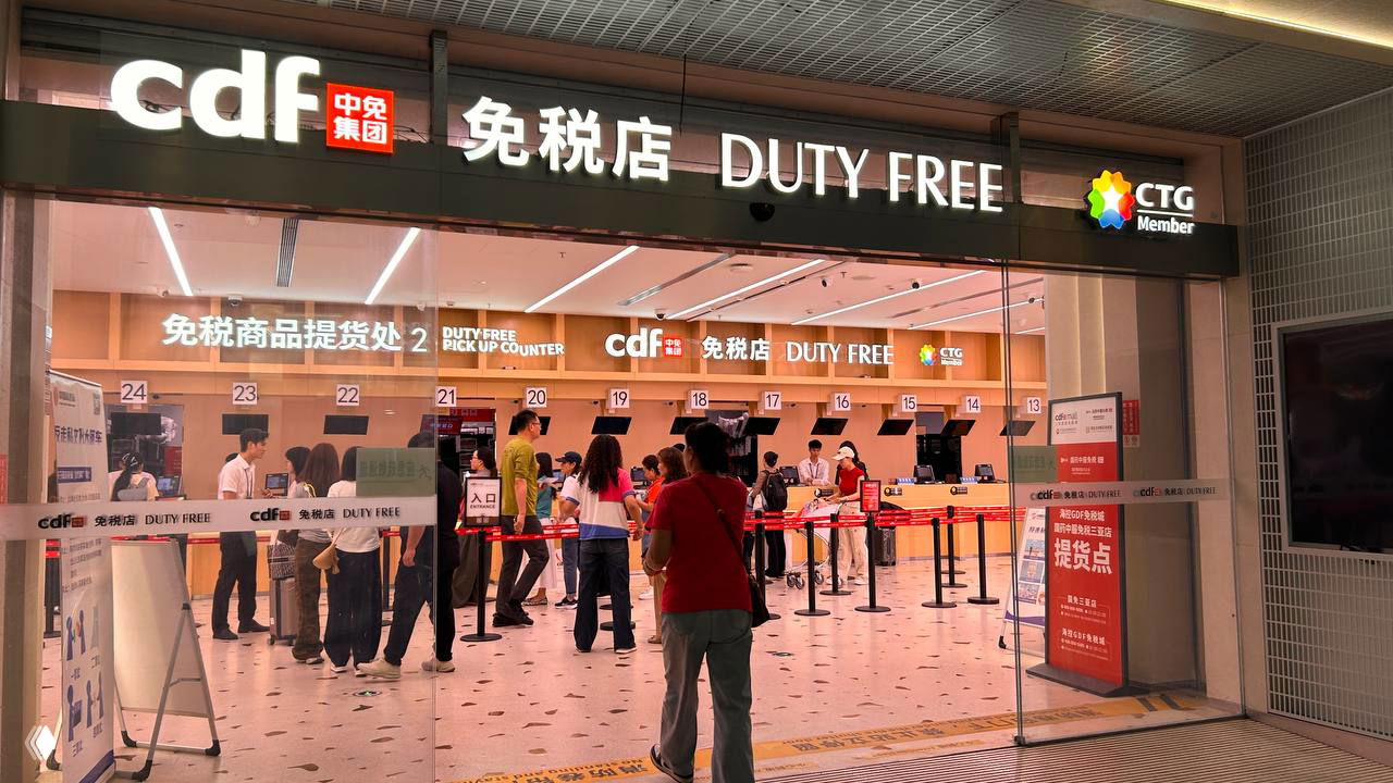 Вход и стойки выдачи Duty Free в аэропорту Саньи: нумерованные пункты выдачи, сотрудники и пассажиры в очереди у pick‑up counter.