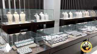 Широкий план витрины ювелирного магазина с рядами подставок, на которых выставлены ожерелья и серьги из натурального жемчуга в стеклянном прилавке.