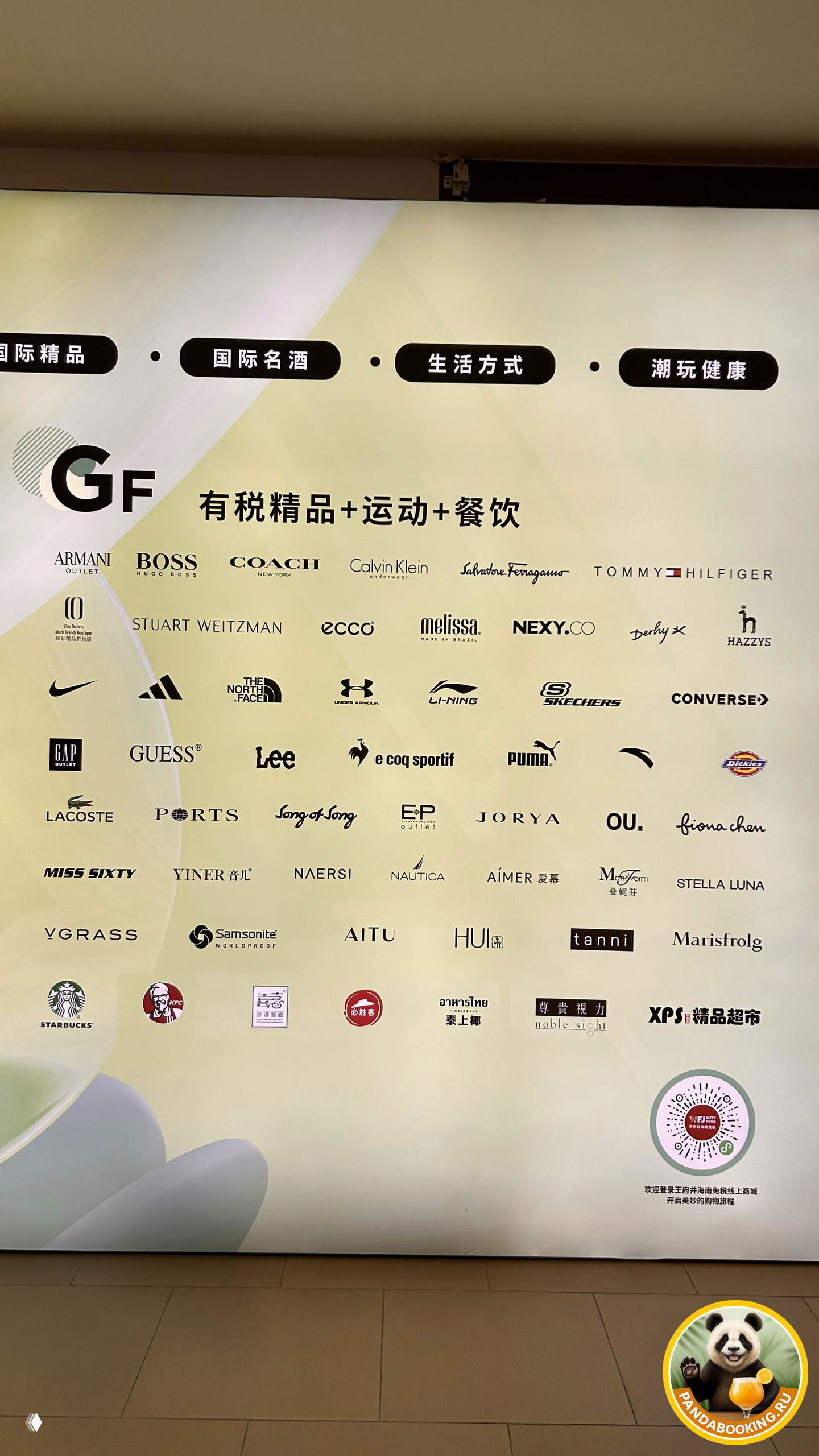 Большая панель со множеством логотипов мировых брендов внутри Wangfujing International Duty Free: вид на бренды одежды и аксессуаров.
