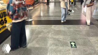 Пол подземного перехода станции метро Гуанчжоу с зелёной стрелкой направления; пассажиры идут, видны сумки и торговые точки по краям.