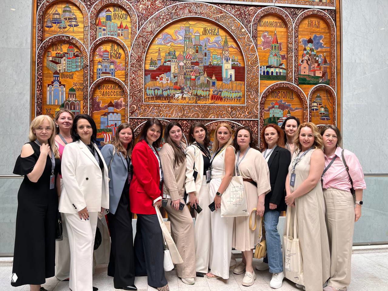 Группа коллег в деловой одежде позирует на фоне декоративной городской панорамы внутри помещения — совместное фото после мероприятия или экскурсии.