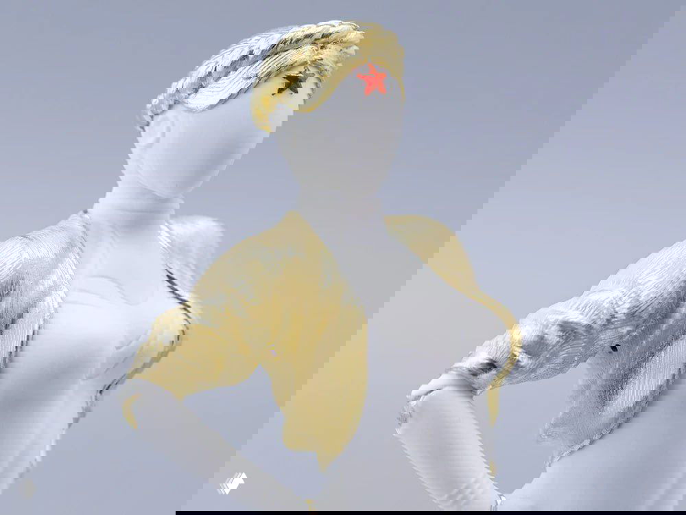 Крупный план фарфоровой фигурки из бисквита в образе Близняшки (Atomic Heart): белая керамика, золочёный жакет и диадема со красной звездой.