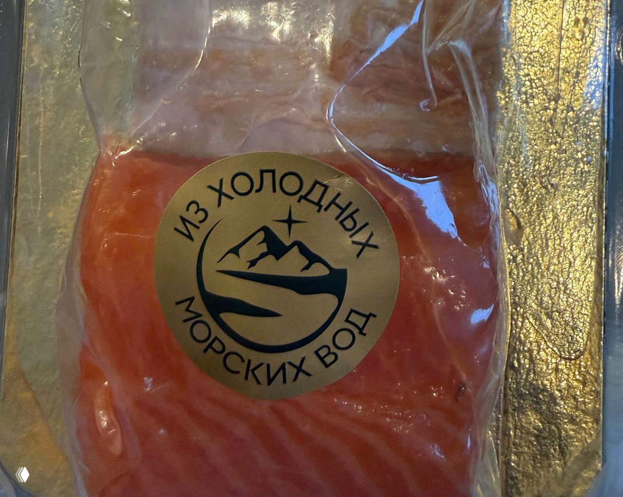 Упаковка филе рыбы в вакуумной упаковке с крупной круглой наклейкой «из холодных морских вод», видно розовое филе и текст маркировки на фоне золотистой окантовки.