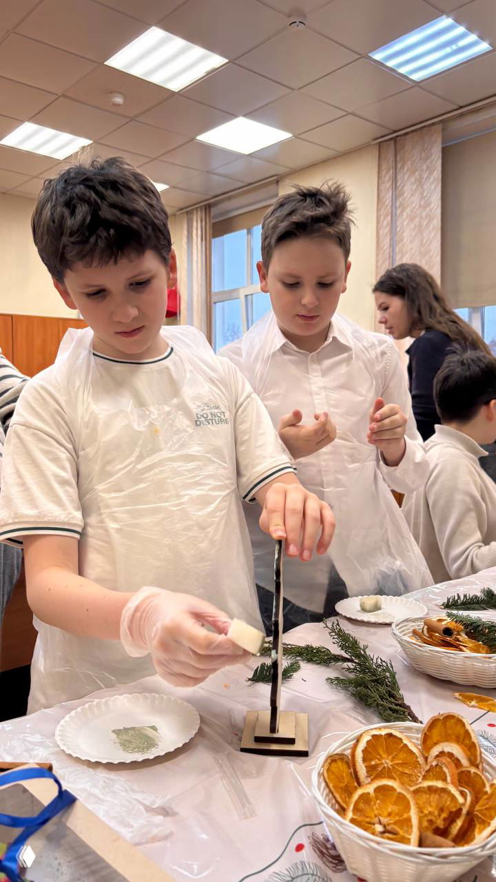 Двое мальчиков в фартуках приклеивают элементы к подставкам ёлочек; рядом миски с сухофруктами и шишками.