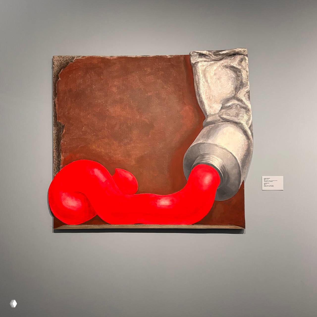 Картина с ярким красным извивающимся объектом и металлическим тюбиком на сером фоне — контрастный образ в экспозиции современного искусства МАММ.