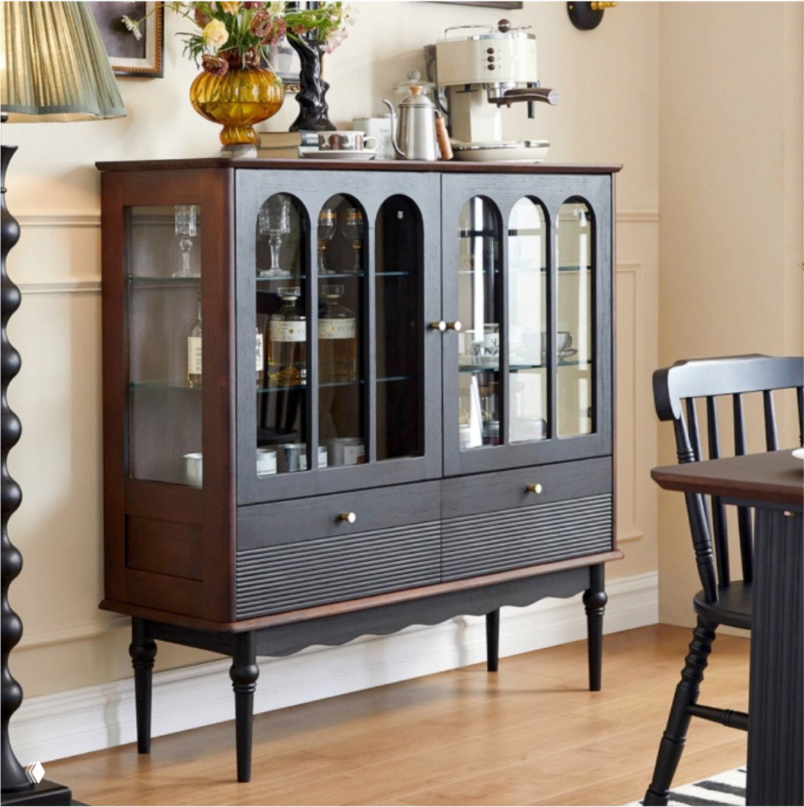 Темный шкаф из массива дуба в интерьере столовой: стеклянные дверцы, полки с посудой и бутылками, декоративные элементы на верхней поверхности, деревянный пол.