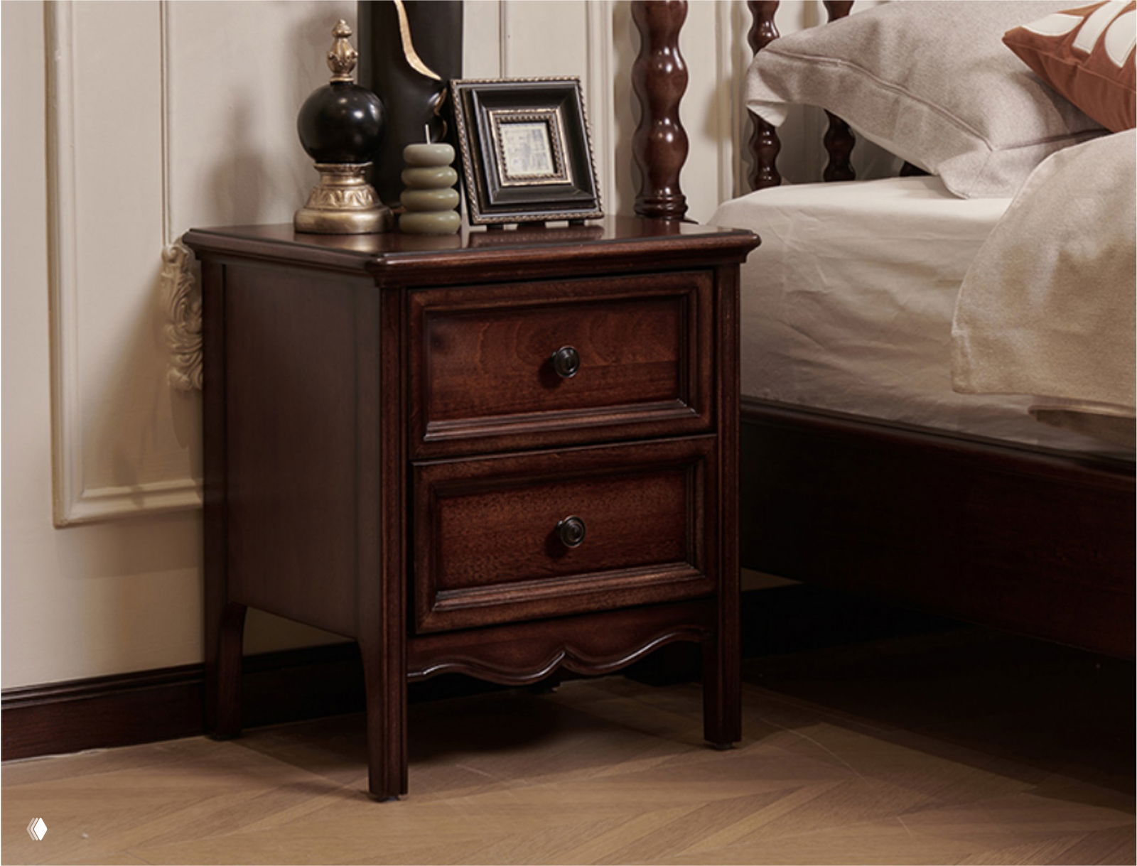 Темная дубовая прикроватная тумбочка в классическом интерьере рядом с кроватью, видна текстура древесины, декоративные элементы и отделка в натуральных тонах.