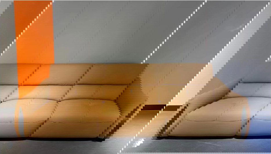 Бежевый трёхместный диван в кожаной/эко-кожаной обивке на выставочном фоне; видны подлокотники, сиденья и силуэт модели.