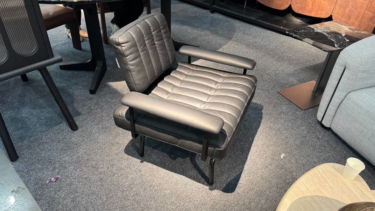 Угловой светлый модульный диван с журнальными столиками и декоративными элементами на фоне стеллажа с интерьерными предметами на выставке.