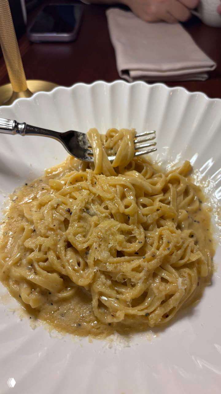 Нежная паста в кремовом соусе (похожая на качо э пепе) в белой тарелке, видно текстуру сыра и вилка в блюде.