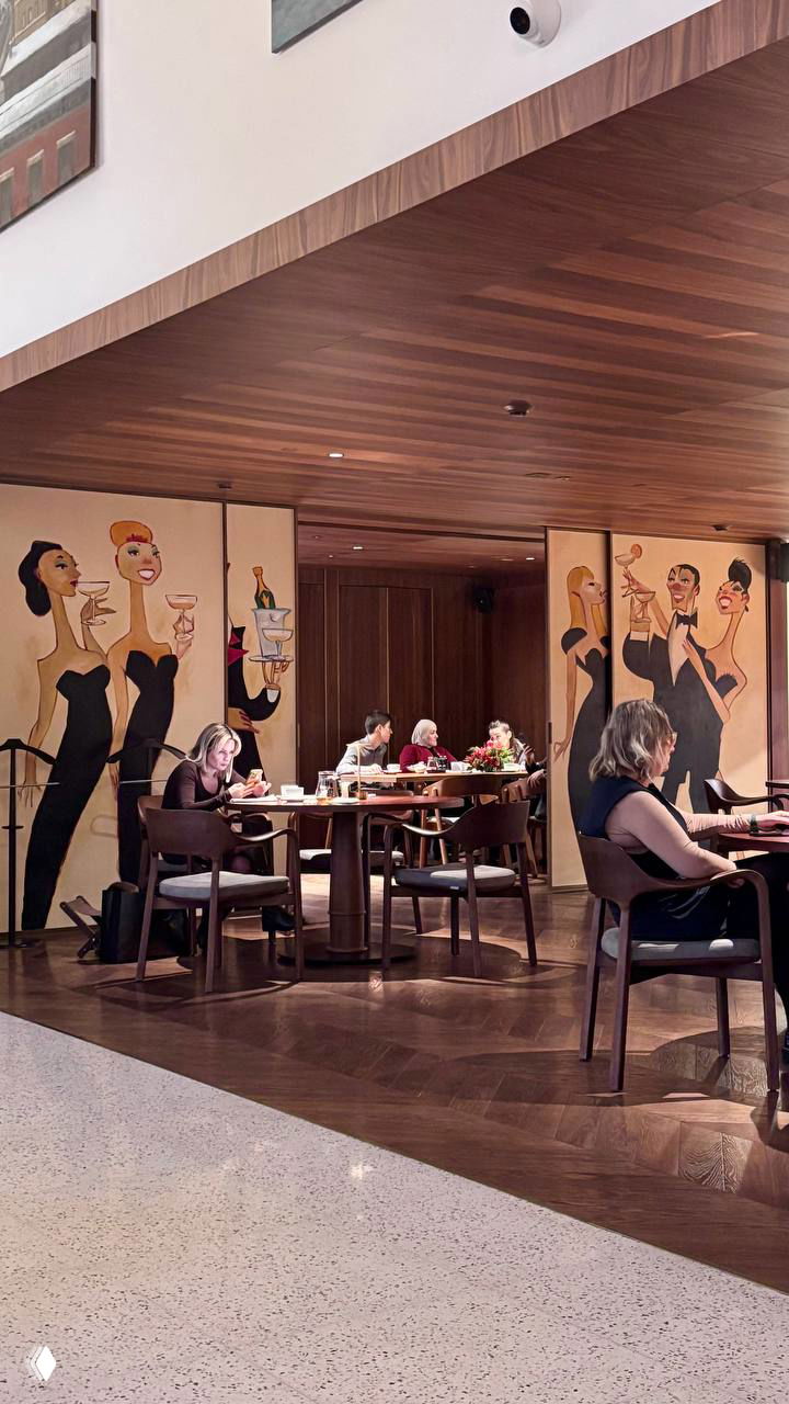 Зал ресторана с деревянным потолком и картинами в стиле ретро; столы, сидящие гости и уютная атмосфера в стиле Нью‑Йорка 70‑х.