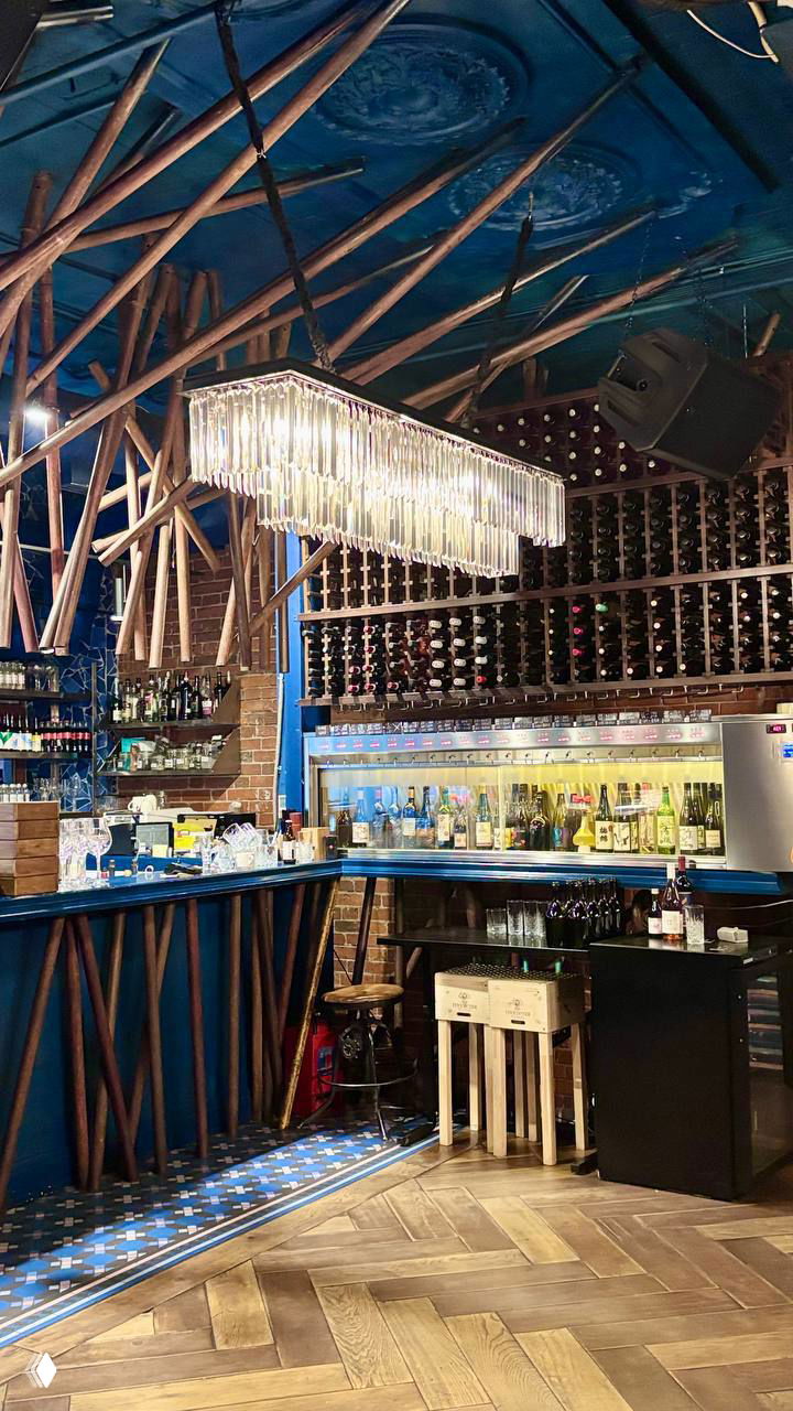 Интерьер бара Single с синей отделкой, хрустальной люстрой и большой винной полкой над стойкой — общая атмосфера заведения и зона эноматика.