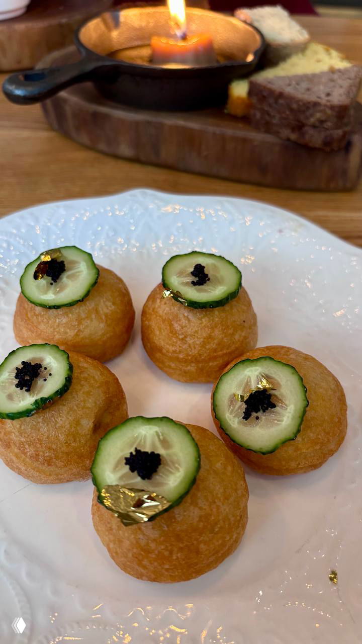 Небольшие закусочные шарики с ломтиком огурца, чёрной икрой и кусочком съедобной золотой фольги на белой тарелке — подача пекарни/ресторана.
