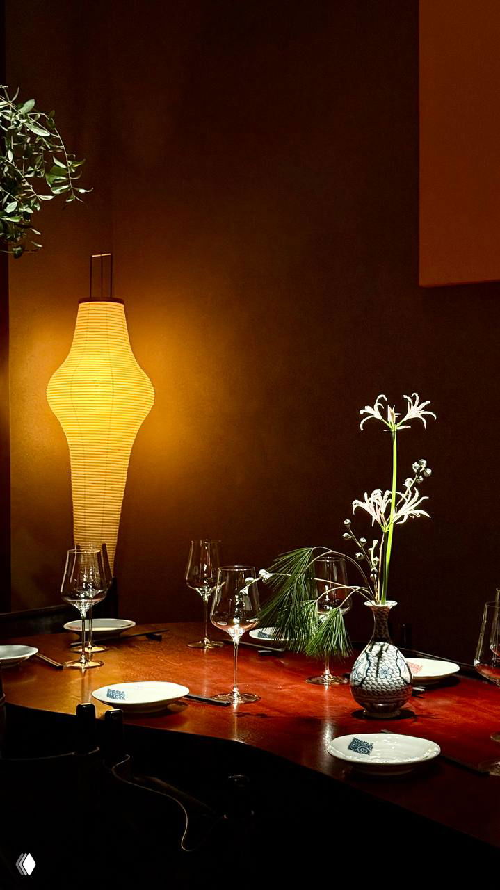 Уголок уютного приватного стола с вазой, стеклянными бокалами и декоративной настольной лампой — спокойная зона для ужина в ресторане.