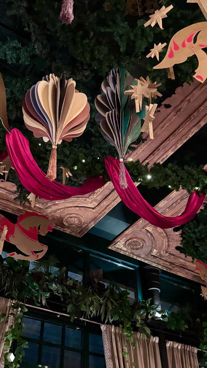 Декор потолка зала Оранжерея: бумажные подвесные украшения, красные драпировки и звёздочки на фоне зелёной растительности